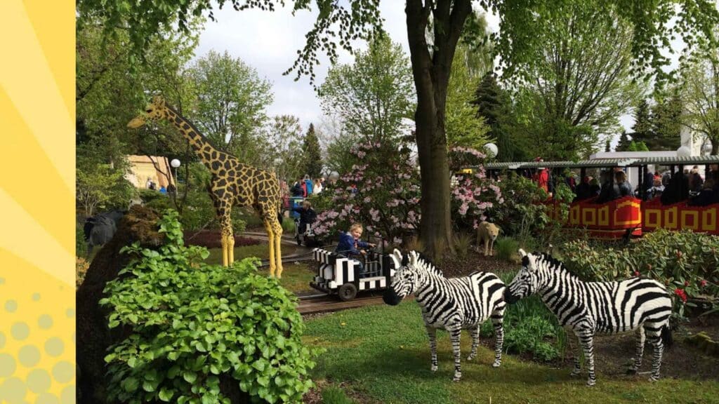 LEGO safaridieren zoals giraffe en zebra's in Legoland Billund, met bezoekers in de miniatuurtrein op de achtergrond