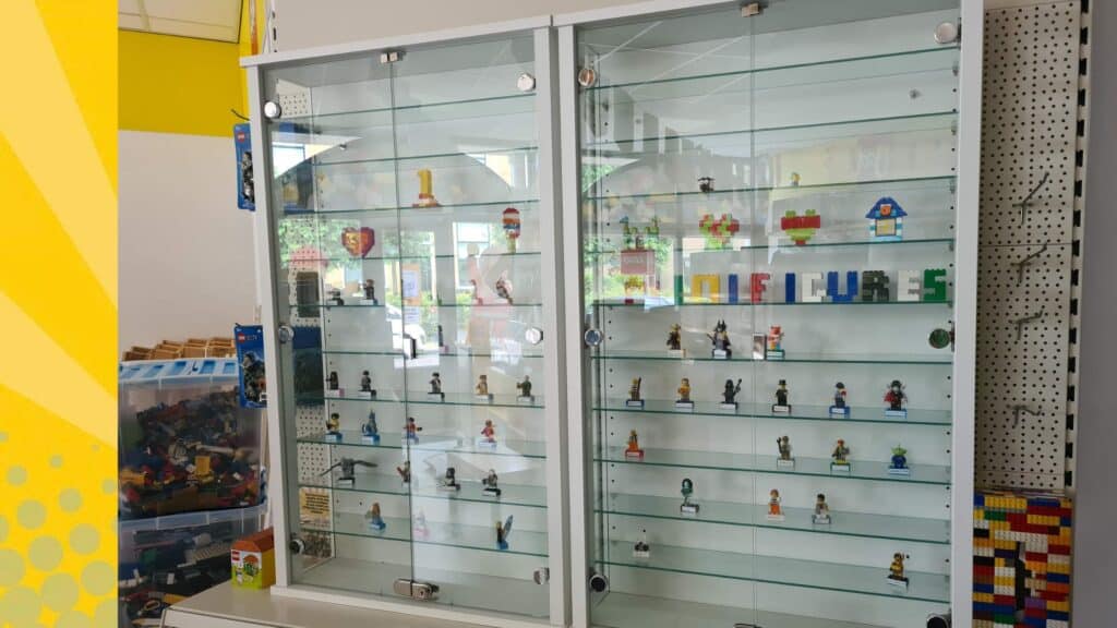 Glazen vitrinekast met LEGO minifiguren op glazen planken, inclusief letterdecoratie