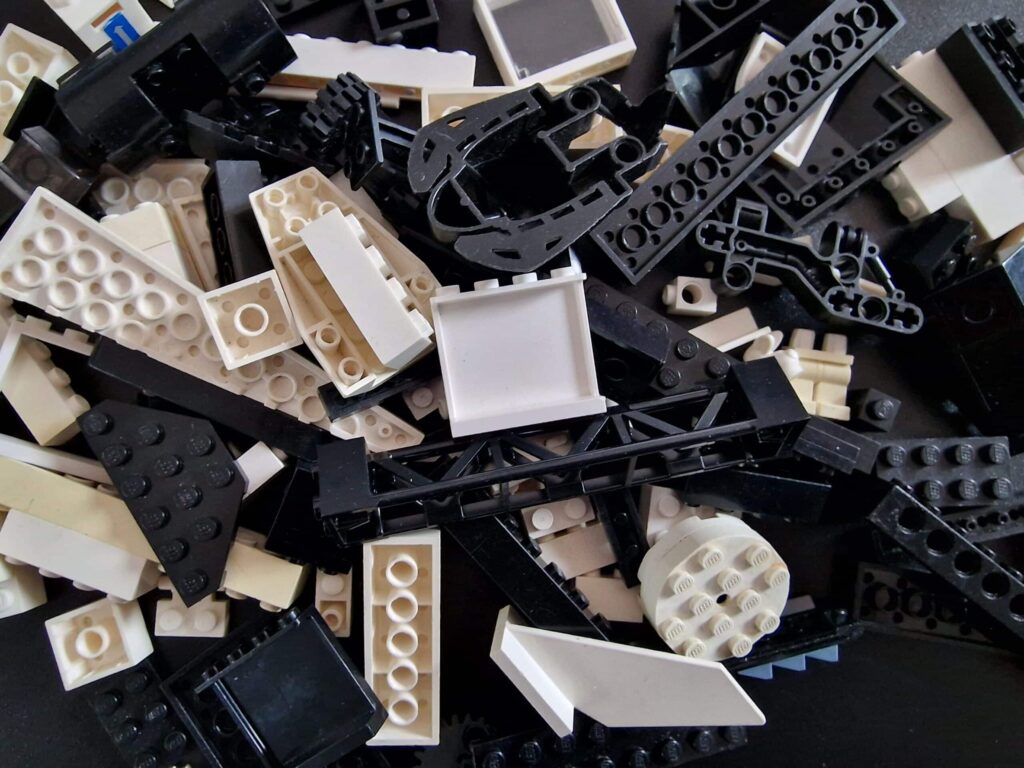 Losse LEGO Technic onderdelen in zwart en wit, waaronder balken, tandwielen en panelen