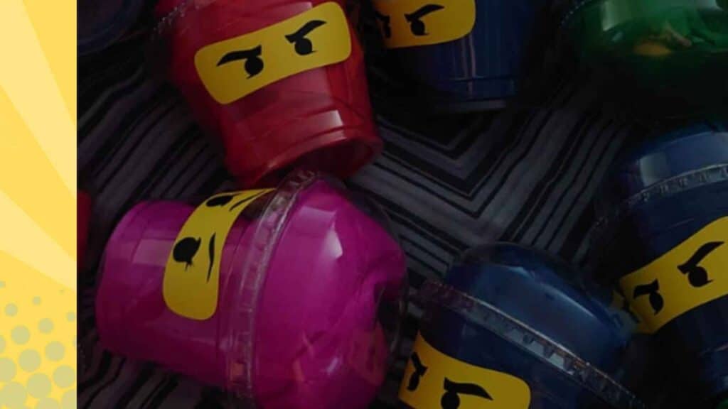 Zelfgemaakte LEGO Ninjago traktatie: gekleurde bekers in rood, blauw, roze en groen met opgeplakte ninja-gezichten